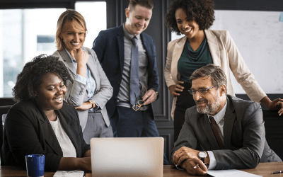 a group of five people smiling around a laptop