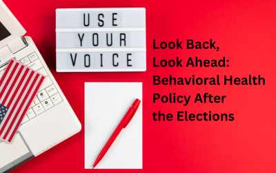 a red background with a laptop on the left with a small US flag on the keyboard, a sign that says 'Use Your Voice', and a notepad and pen. Text reads 'Look Back, Look Ahead: Behavioral Health Policy After the Elections'