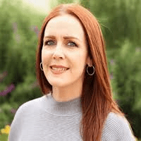 a middle-aged white woman with long red hair wearing a light grey sweater