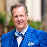 aan older white man wearing a bright blue suit with a tree in the backgroun