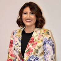 a white woman with shoulder-length brown hair wearing a blazer with flowers on it