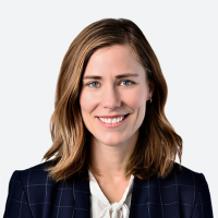 a white woman with shoulder-length light brown hair, wearing a dark blue blazer over a white top