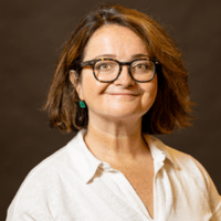 a white woman with short straight brown hair, wearing glasses, green earrings, and a white button-up top