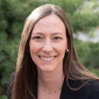 a white woman with long straight light brown hair wearing a black top with a necklace