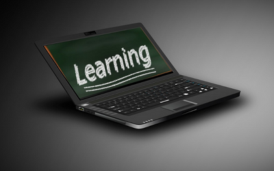 a photo of an older laptop, with a green chalkboard on screen with the word 'Learning' on it